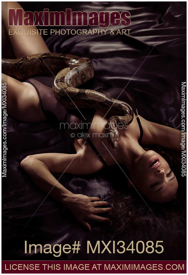 Beautiful seductive woman lying in an ecstatic pose on a bed with a large boa constrictor snake on her sensual body