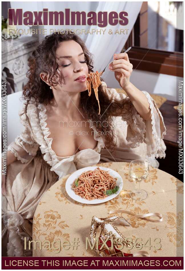 Beautiful sensual woman in vintage Venetian carnival dress eating pasta with passion sitting at restaurant table