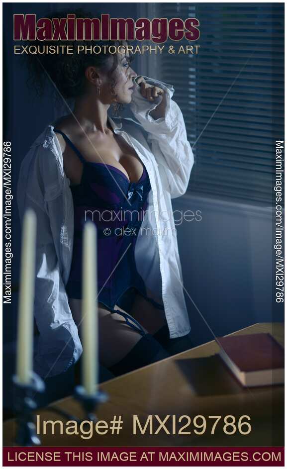 Beautiful sexy woman in a men's shirt on top of a corset sitting by the window at night