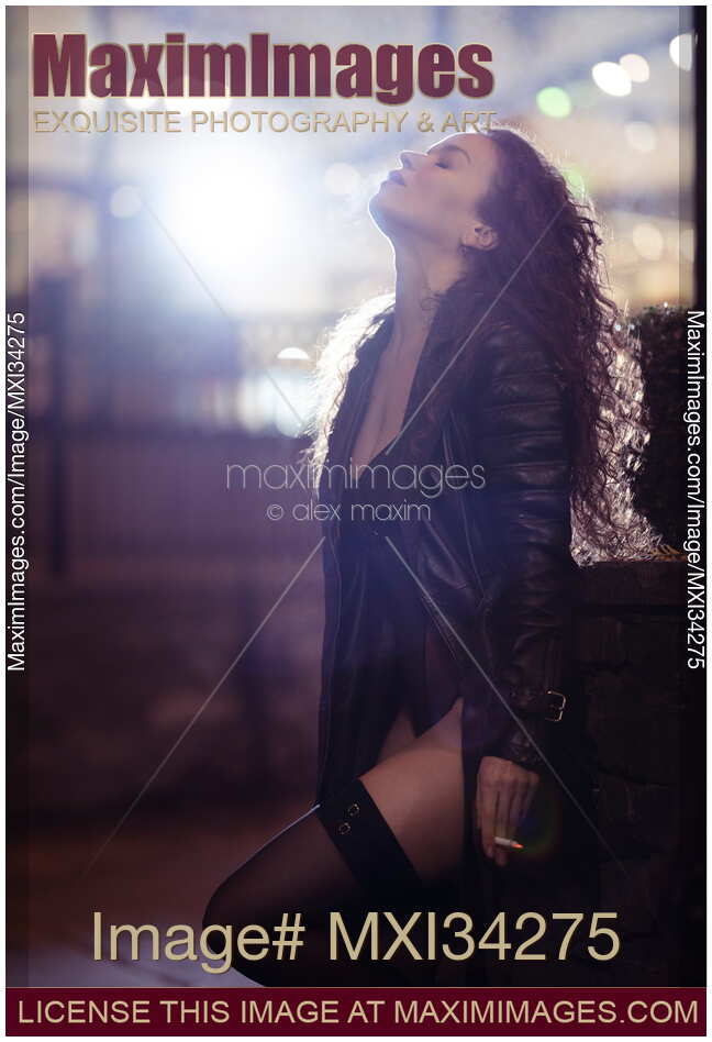 Beautiful sexy woman in black exhaling cigarette smoke with abandon and relief on night city street