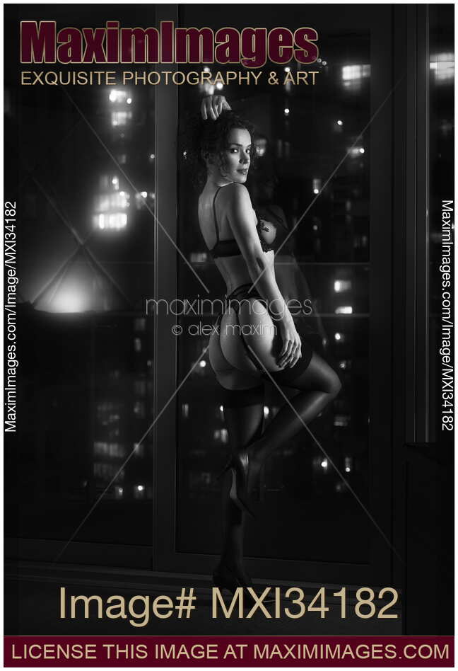 Beautiful sexy woman in lingerie and stockings dancing in front of a window in night city view Black and white noir