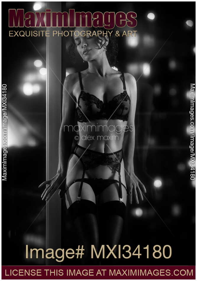 Beautiful sexy woman in lingerie dancing in front of a window with glowing city night lights taking off her underwear Black and white