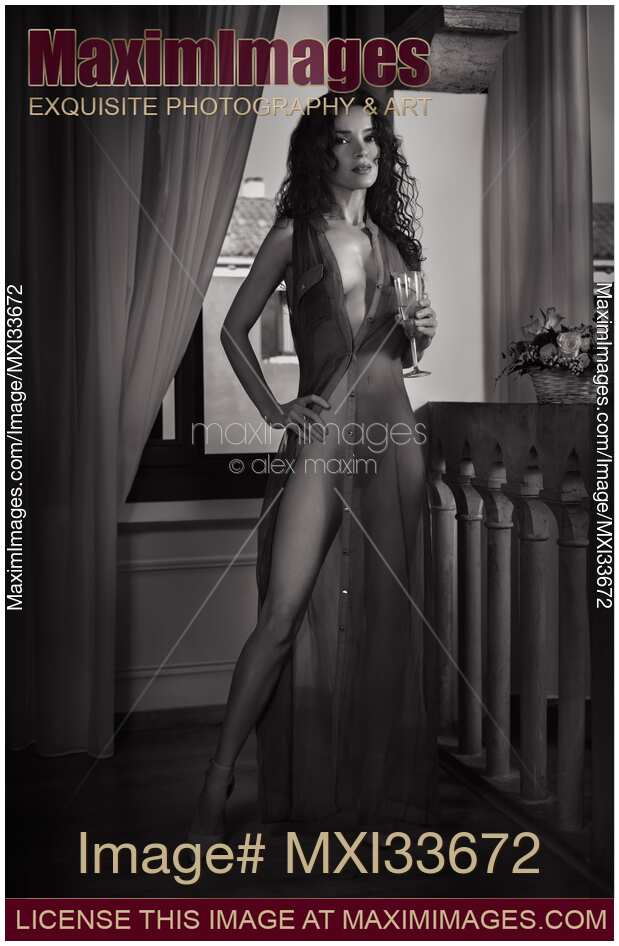 Beautiful sexy woman in sheer unbuttoned dress revealing her naked body standing with a glass of wine. Black and white.