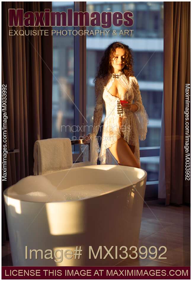 Beautiful sexy woman in white sheer lace night gown standing by a bath tub in luxurious bathroom