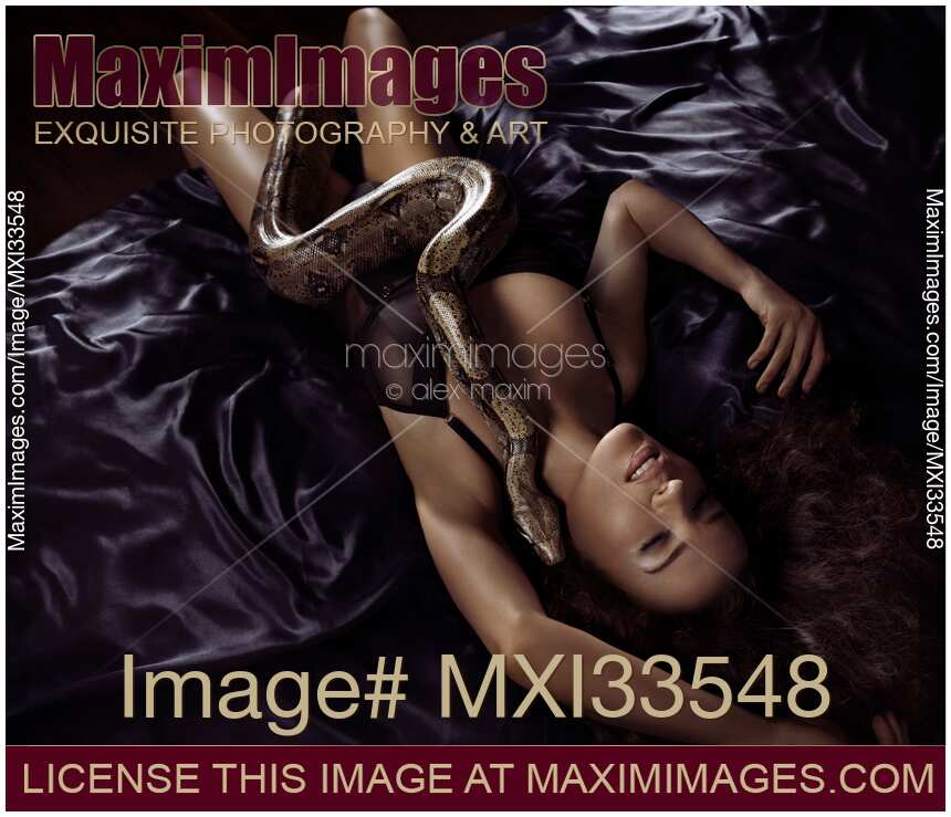 Beautiful sexy woman lying on silky bed in ecstatic pose with large Kundalini boa snake whispering in her ear