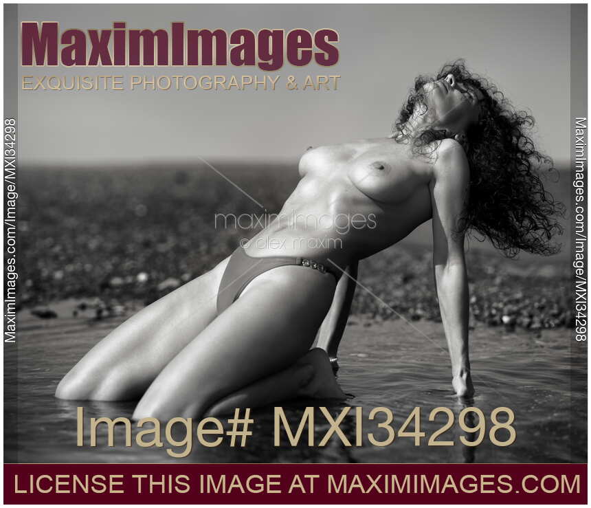 Beautiful sexy woman posing topless in bikini kneeling in shallow sea water arching her body Black and white