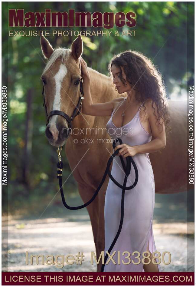 Beautiful sexy woman rider in elegant dress caressing a horse in nature with tranquil expression