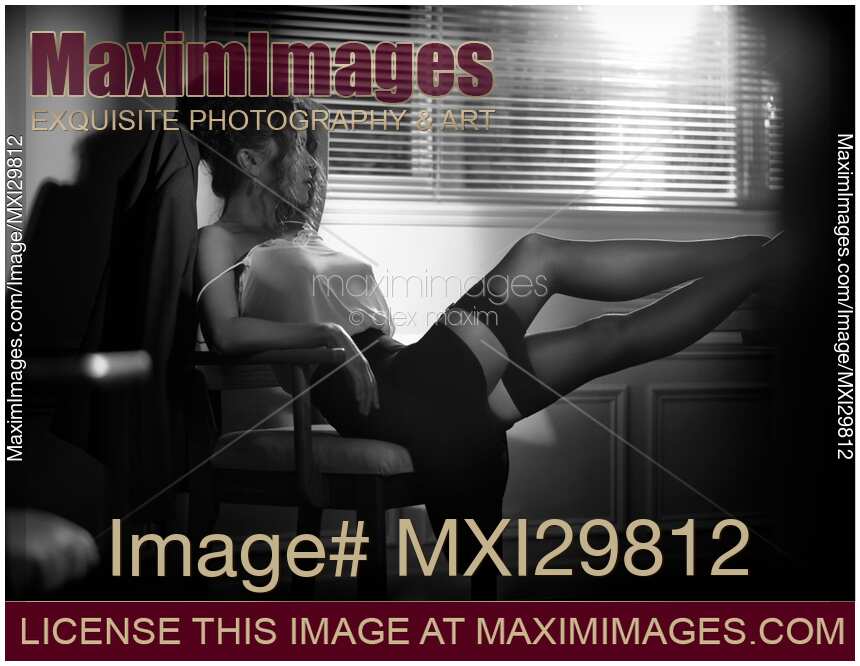 Beautiful sexy woman sitting with her legs in stockings on a desk in dim night light by the window Black and white