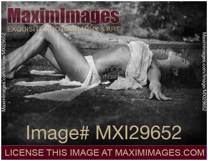 Beautiful sexy young woman lying on the ground under pouring rain