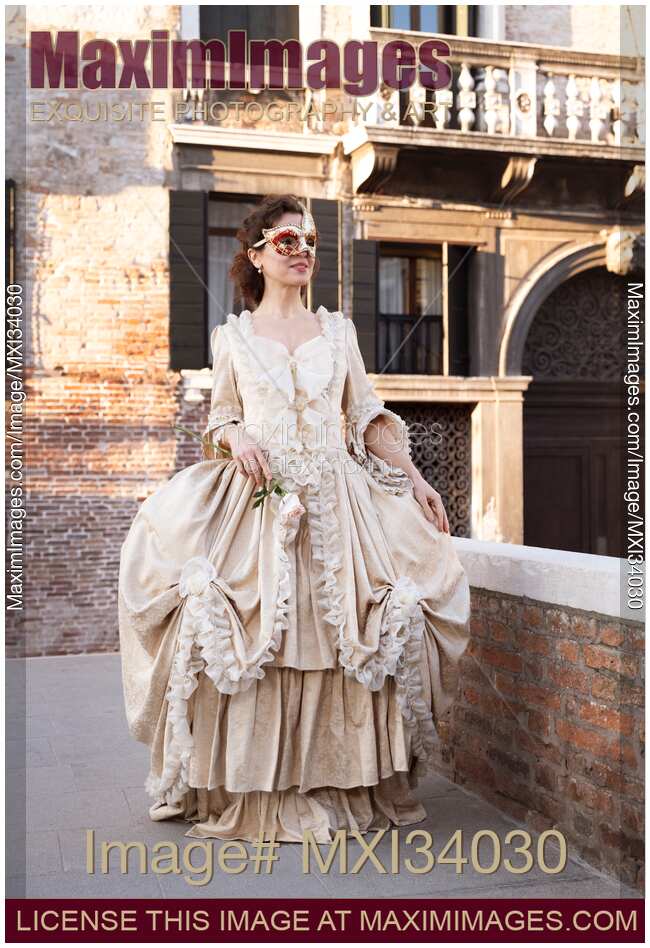 Beautiful smiling lady in vintage Italian carnival costume dress and mask walking along historic street in Venice