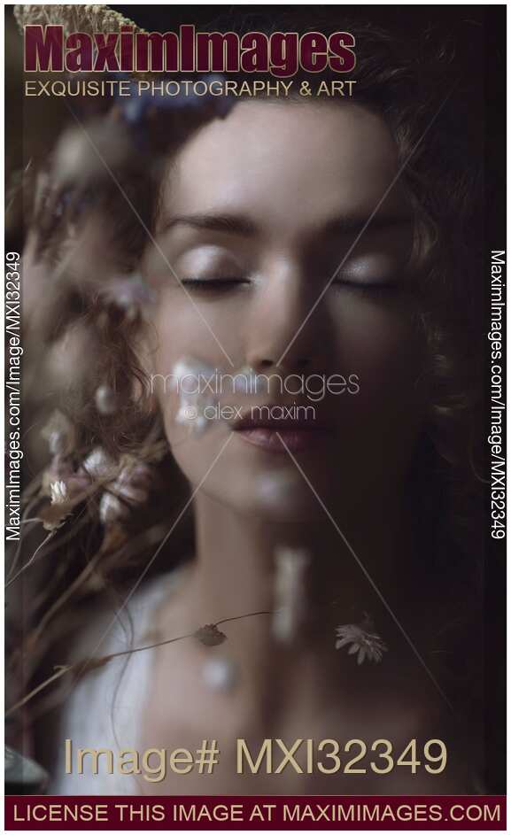 Beautiful tranquil woman face with closed eyes behind wild flowers dreamy portrait