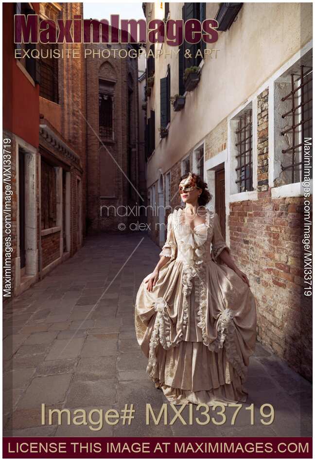 Beautiful Venetian lady in vintage dress and carnival mask walking along historic city street in Venice