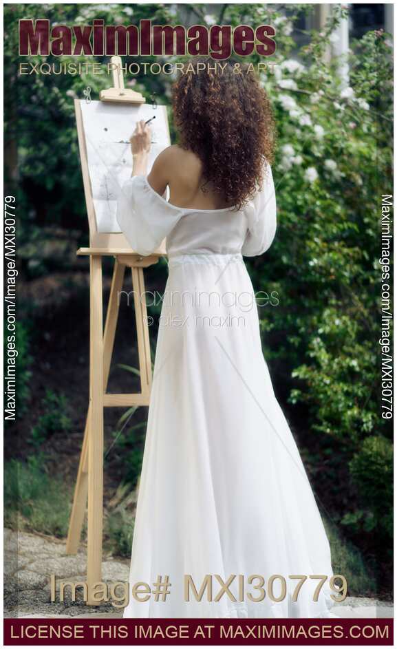 Beautiful woman artist with an easel painting outdoors in a garden in sheer white gown