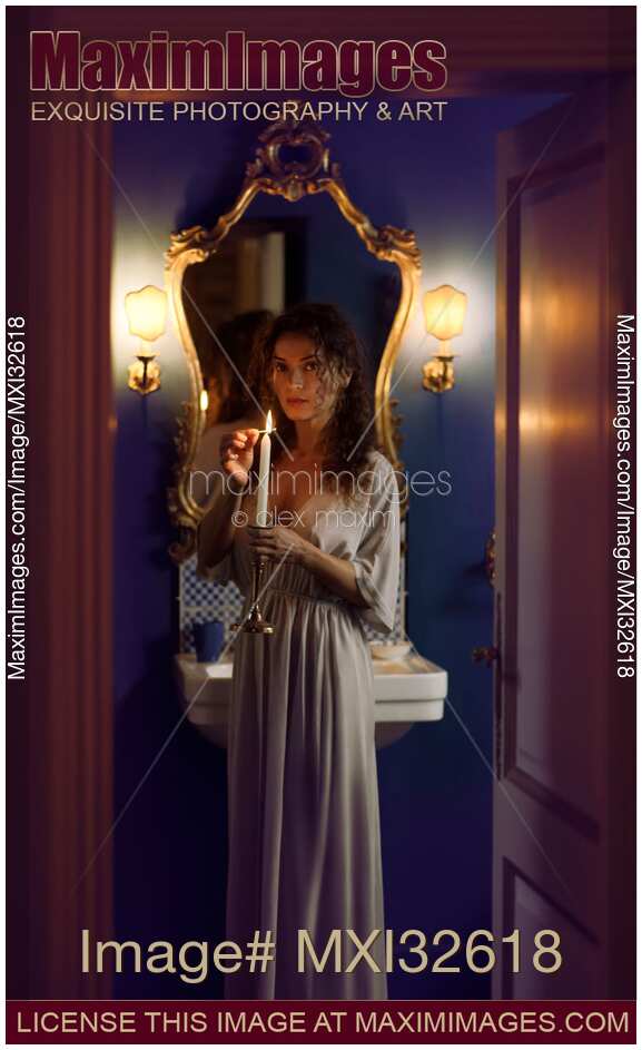Beautiful woman in evening gown lighting a candle in her hand with an expressive mysterious look in bathroom settings