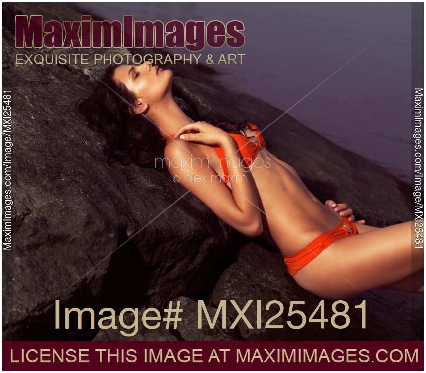 Beautiful woman in orange bikini lying on rock near water