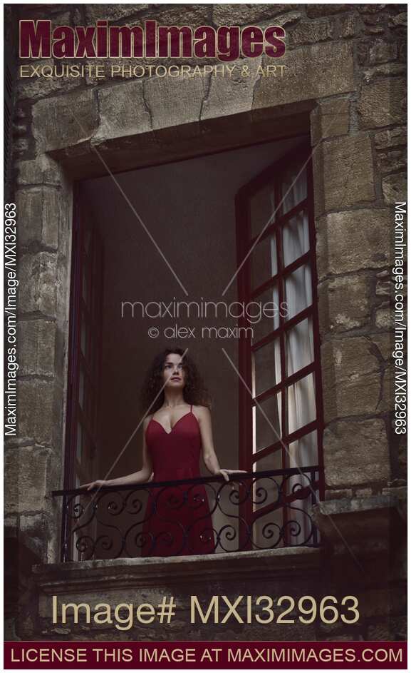 Beautiful woman in red dress standing in open window of medieval French house looking outside