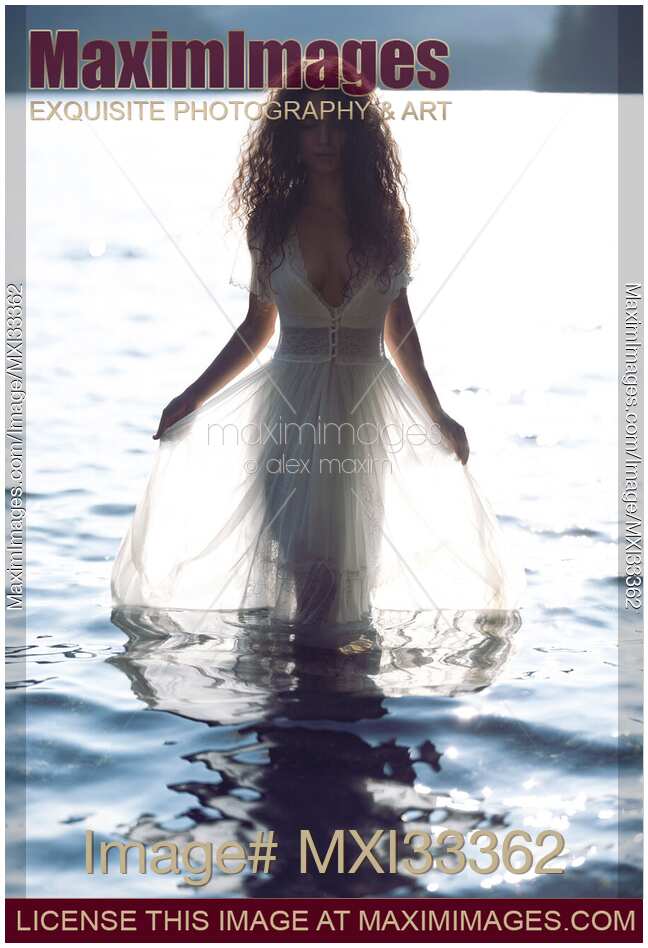 Beautiful woman in sheer white lace dress walking out of water like a Greek Goddess