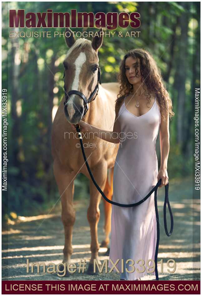 Beautiful woman inelegant silvery silk dress walking with a horse along the forest trail