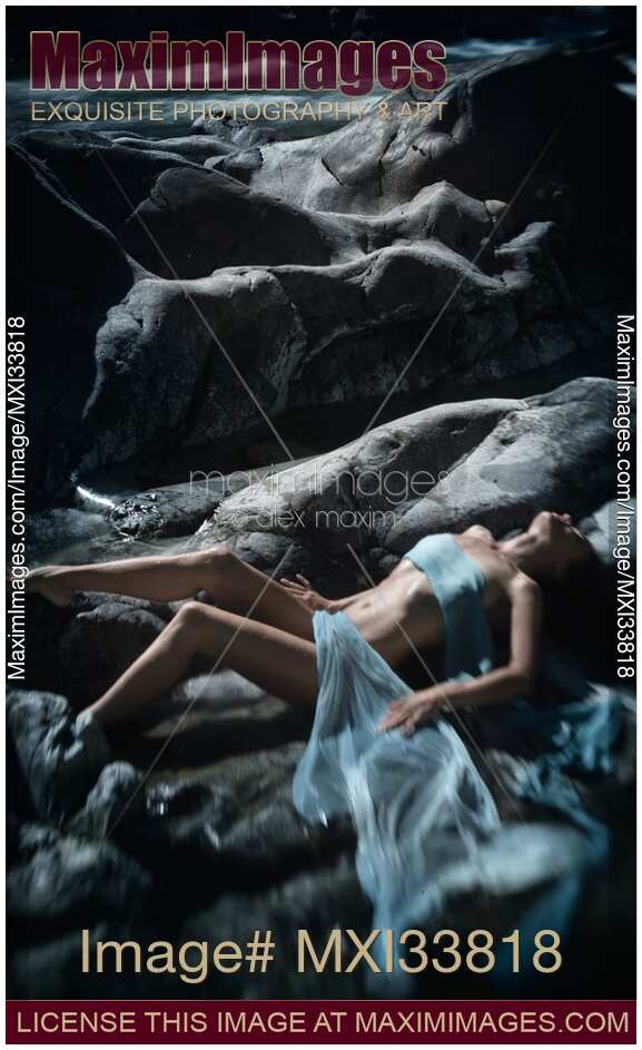 Beautiful woman lying on smooth river rocks with her barely covered sensual body in dramatic outdoor nature scenery