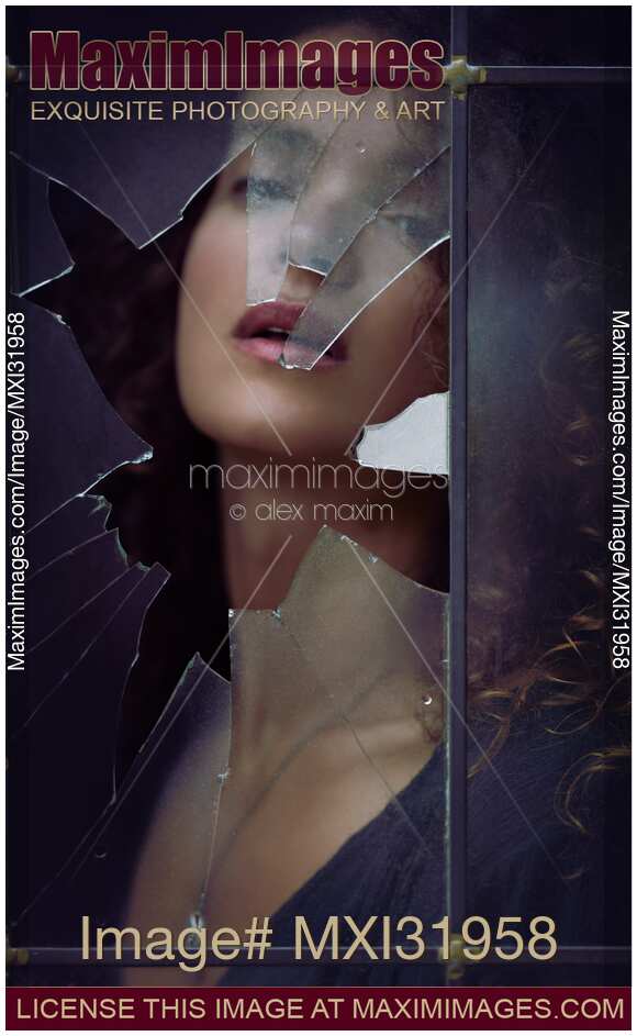 Beautiful woman sensual face behind a broken window shattered glass in a dark house