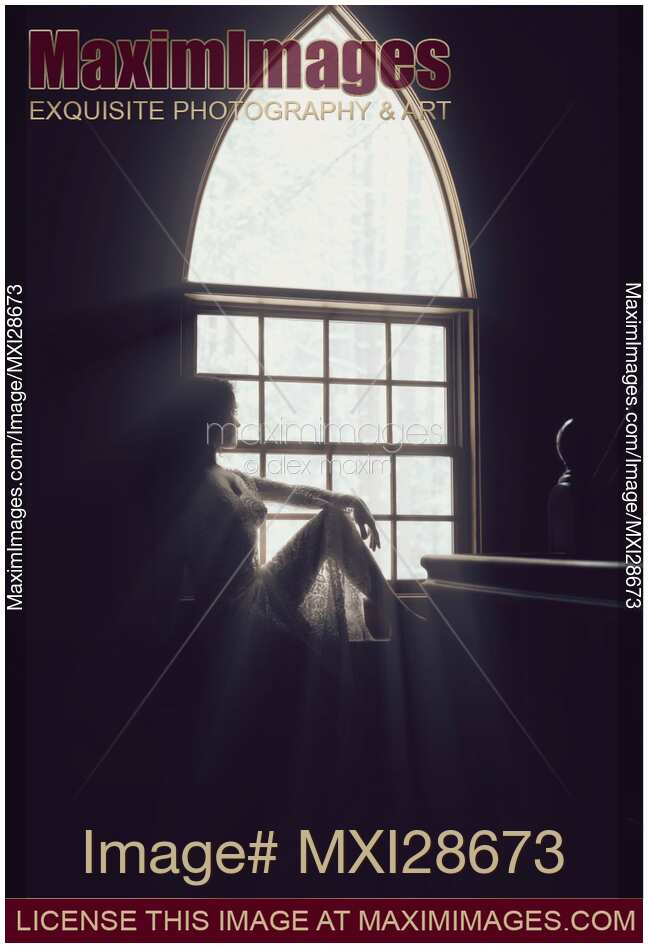 Beautiful woman sitting on a window sill in bright sunlight
