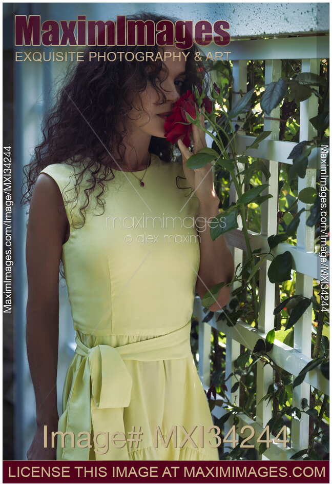 Beautiful woman with an expressive deep gaze smelling a red rose in a dimly lit garden
