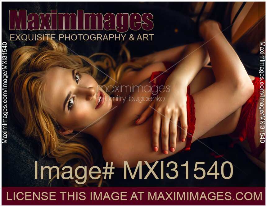 Beautiful woman with blond hair and a seductive smile lying in sexy red lingerie