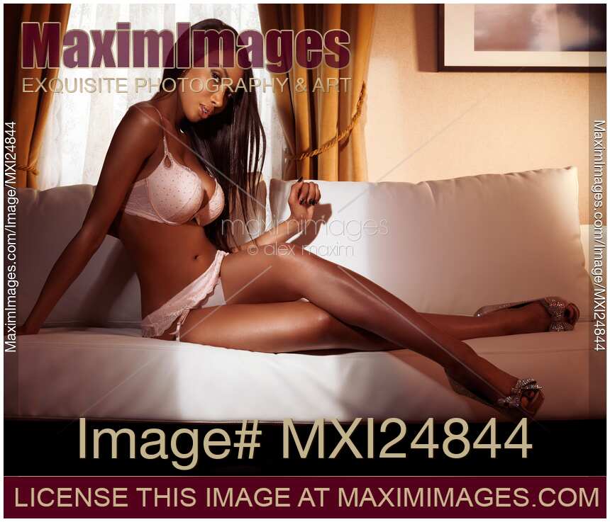 Beautiful young black woman in pink lingerie sitting on sofa