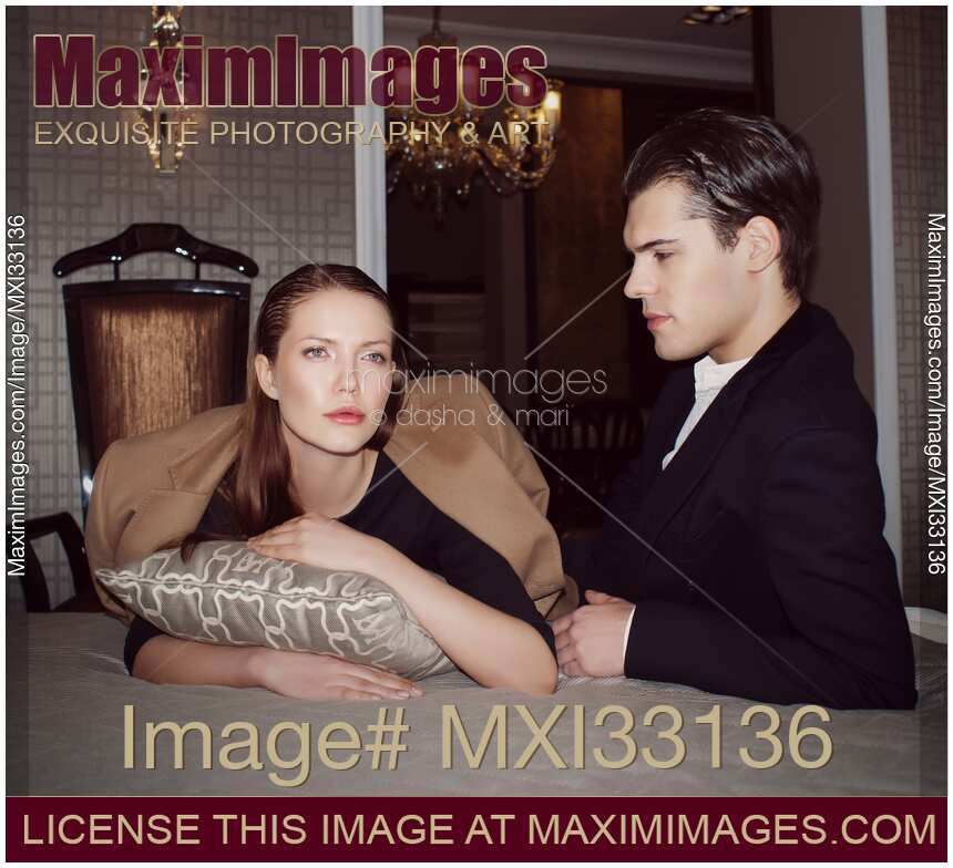 Beautiful young romantic couple in elegant classic clothes lying on a bed in a luxury hotel suite