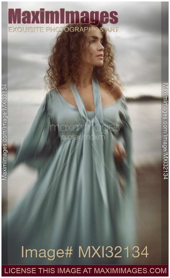 Beautiful young woman in a blue dress standing on the ocean shore with a thoughtful expressive look