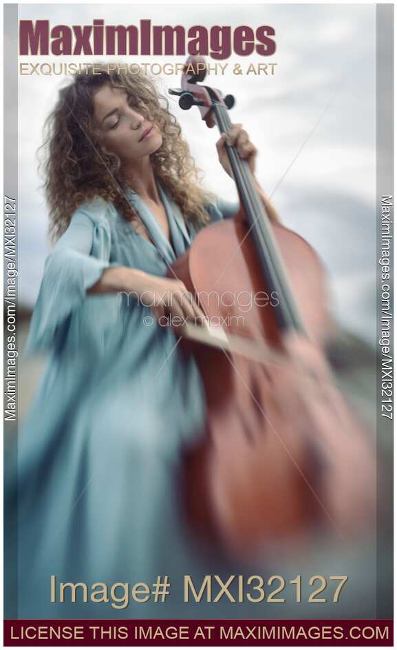 Beautiful young woman in a blue vintage dress passionately playing cello in sunrise nature scenery
