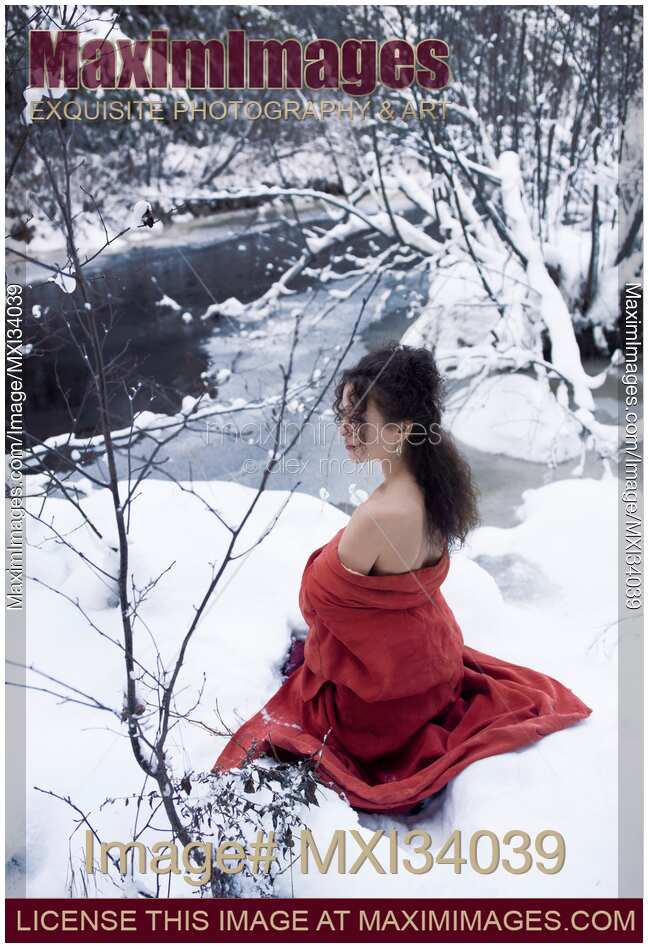 Beautiful young woman in red kimono sitting in snow by a frozen river with bared shoulders