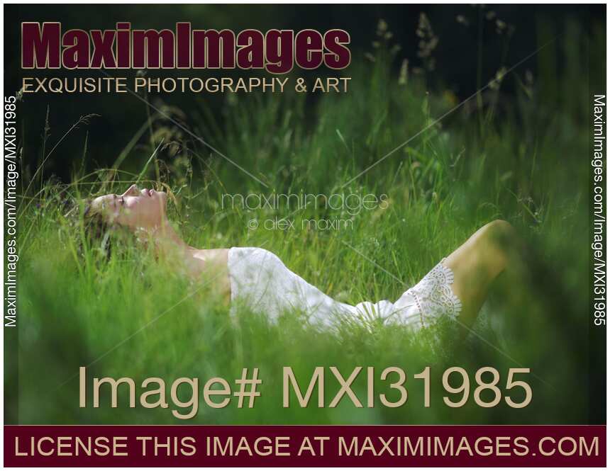 Beautiful young woman in summer dress lying in green grass in a sunny nature scenery