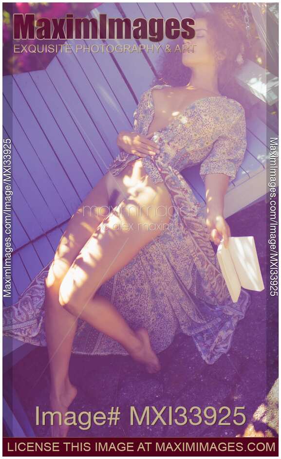 Beautiful young woman lying asleep on garden bench with book in her hand and unbuttoned dress revealing her naked body