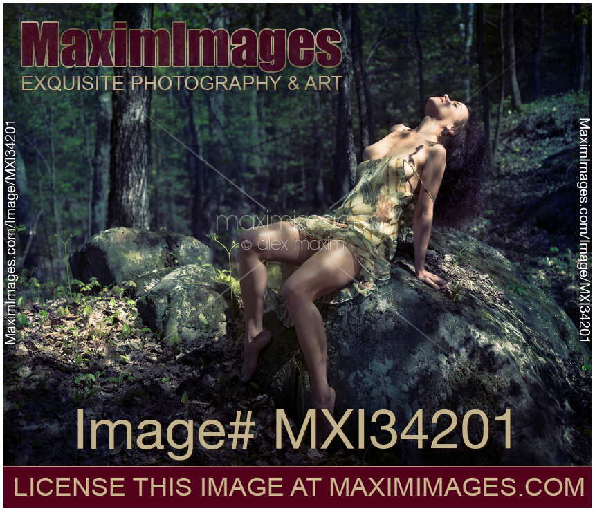 Beautiful young woman sitting on a rock in a forest in a sensual relaxed pose with her dress undone revealing her legs and breast