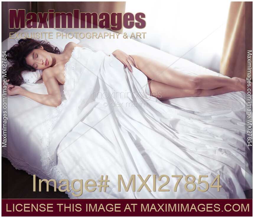 Beautiful young woman sleeping naked in bed covered with white sheets