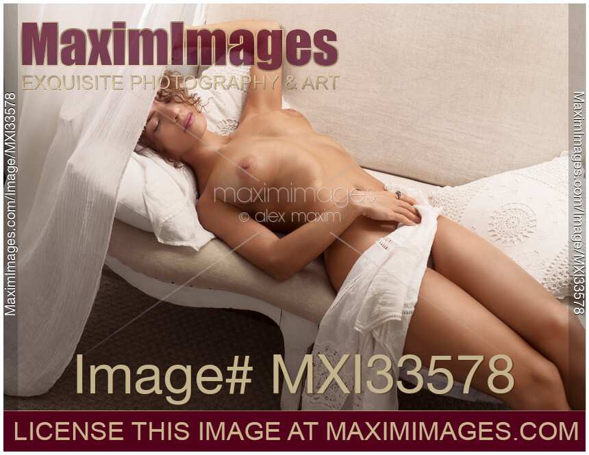 Beautiful young woman sleeping naked on a sofa in a carefree relaxed sensual pose with bright daylight on her bare skin