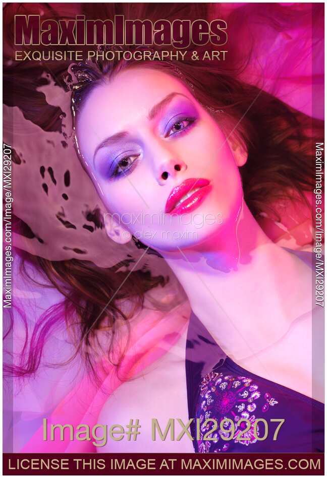 Beauty face portrait of woman lying in water with makeup in vivid pink purple colored light
