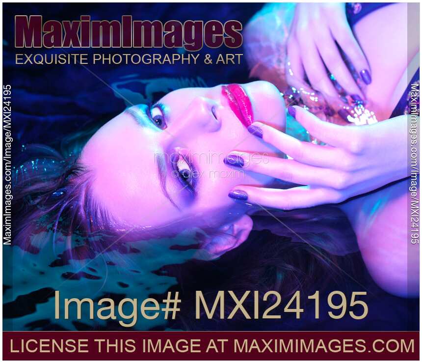 Beauty portrait of woman lying in water with purple makeup and manicure under colorful lighting