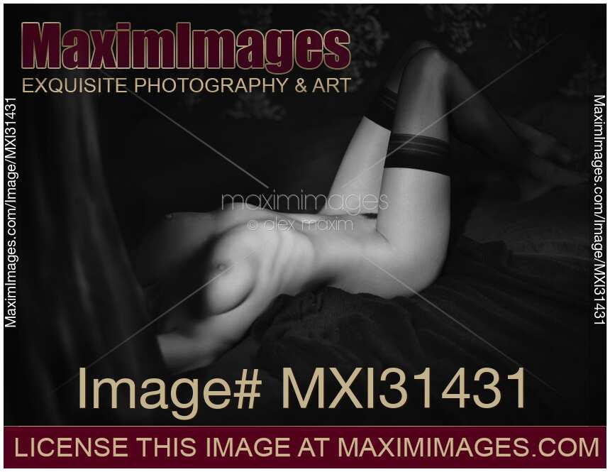 Black and white art nude body portrait of a woman in stockings lying in bed naked obscured by shadows