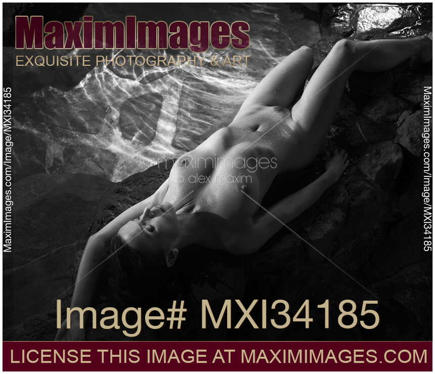 Black and white art nude photograph of a gorgeous woman with beautiful wet sexy naked body lying on rocks by an onsen hot spring bath