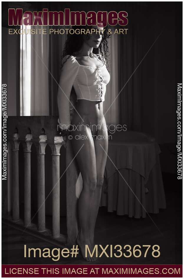 Black and white art nude portrait of a beautiful woman standing half-naked wearing only a top revealing her nudity in dark room