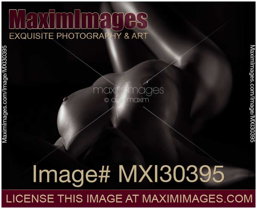 Black and white art nude portrait of a sexy woman with her body lit by dim light closeup of breasts with oily skin
