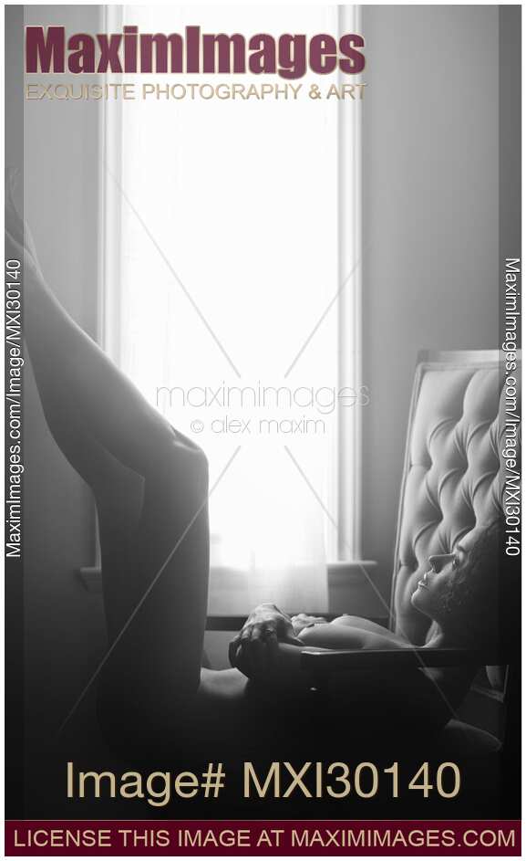 Black and white art nude portrait of beautiful woman lying naked in armchair with her legs raised