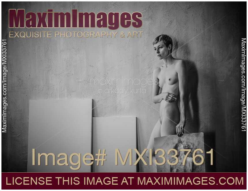 Black and white art nude portrait of woman artist standing naked with a painting leaning against wall