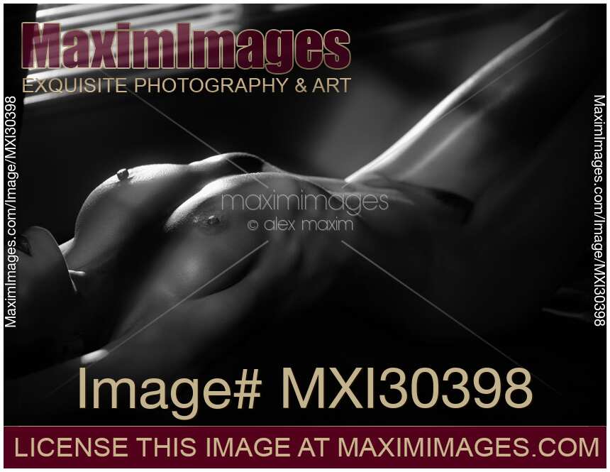 Black and white Art nude woman lying with her sexy naked body outline lit by dim night light and hidden by shadows