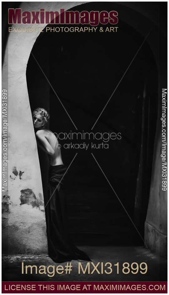 Black and white artistic half-nude portrait of a young woman leaning against archway wall