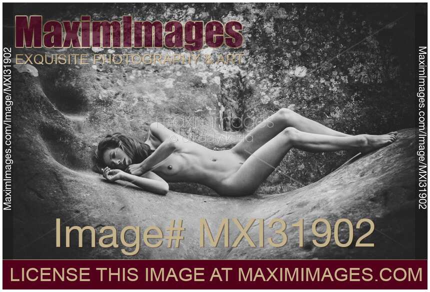 Black and white fine art nude photograph of a skinny young woman lying naked on rocks