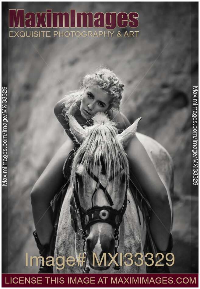 Black and white portrait of a beautiful young woman sitting naked on a horse