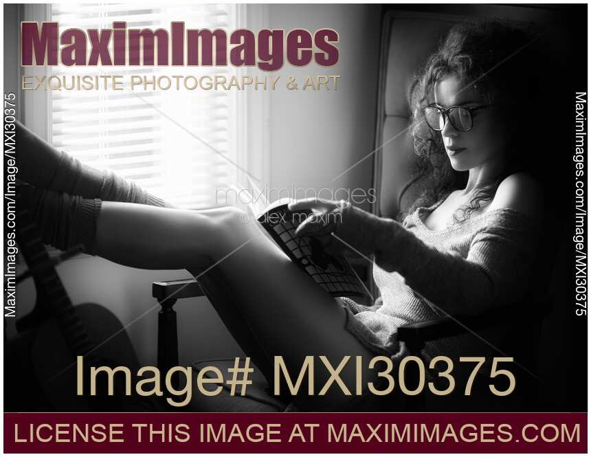 Black and white portrait of a sexy woman in large reading glasses at home with a book